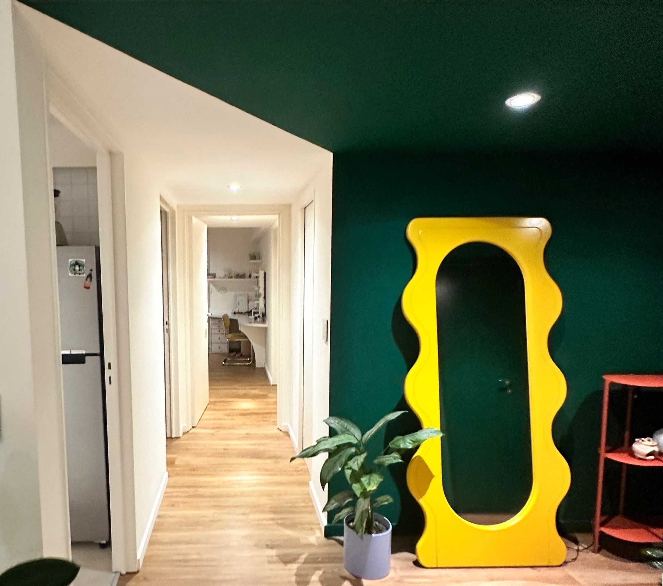 Pasillo del proyecto Charlone con un espejo de piso ondulado en amarillo contra una pared verde profundo