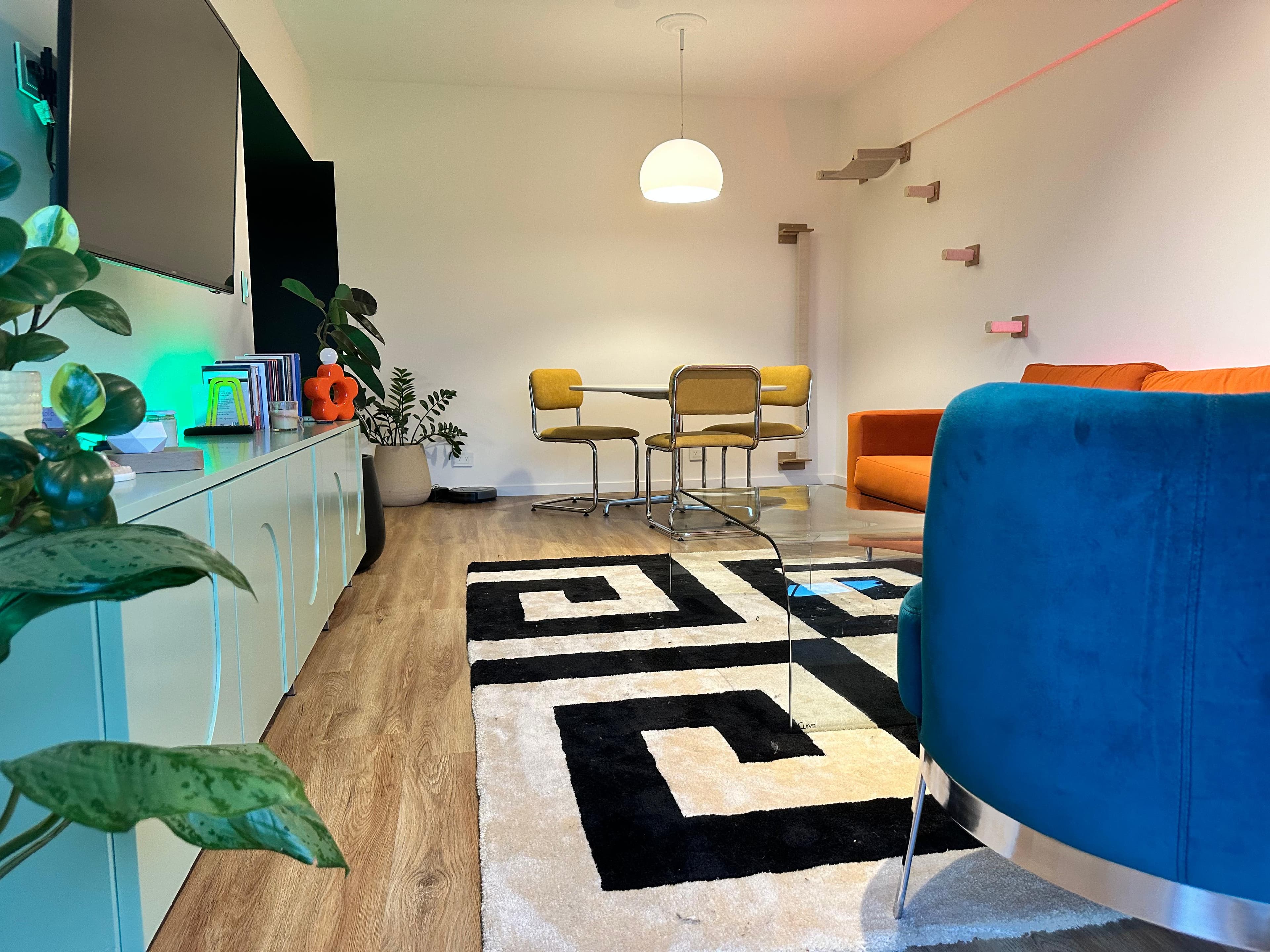 Living comedor con sillones azul y naranja, mesa redonda y sillas amarillas sobre alfombra con greca